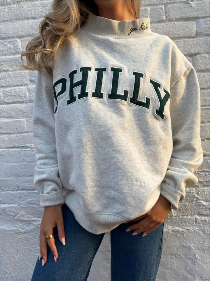 Dame med vid skåret college-sweatshirt med høj krave og påsyet skrift Skovae