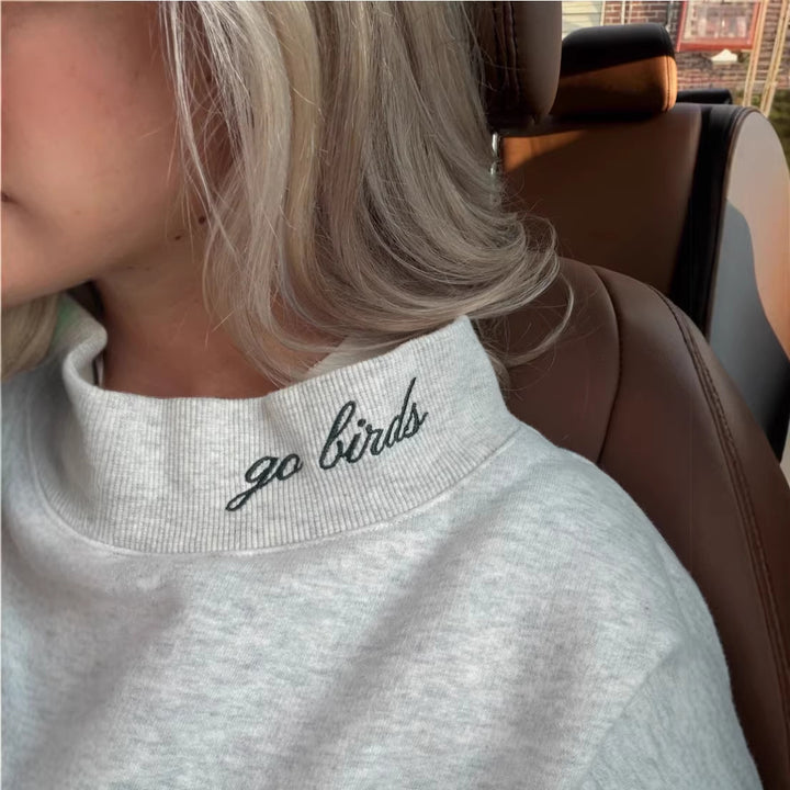 Dame med vid skåret college-sweatshirt med høj krave og påsyet skrift Skovae