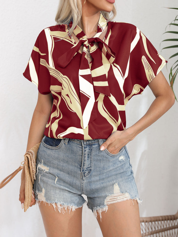 Damebluse med flot sløjfekrave og moderne grafisk design Stilla